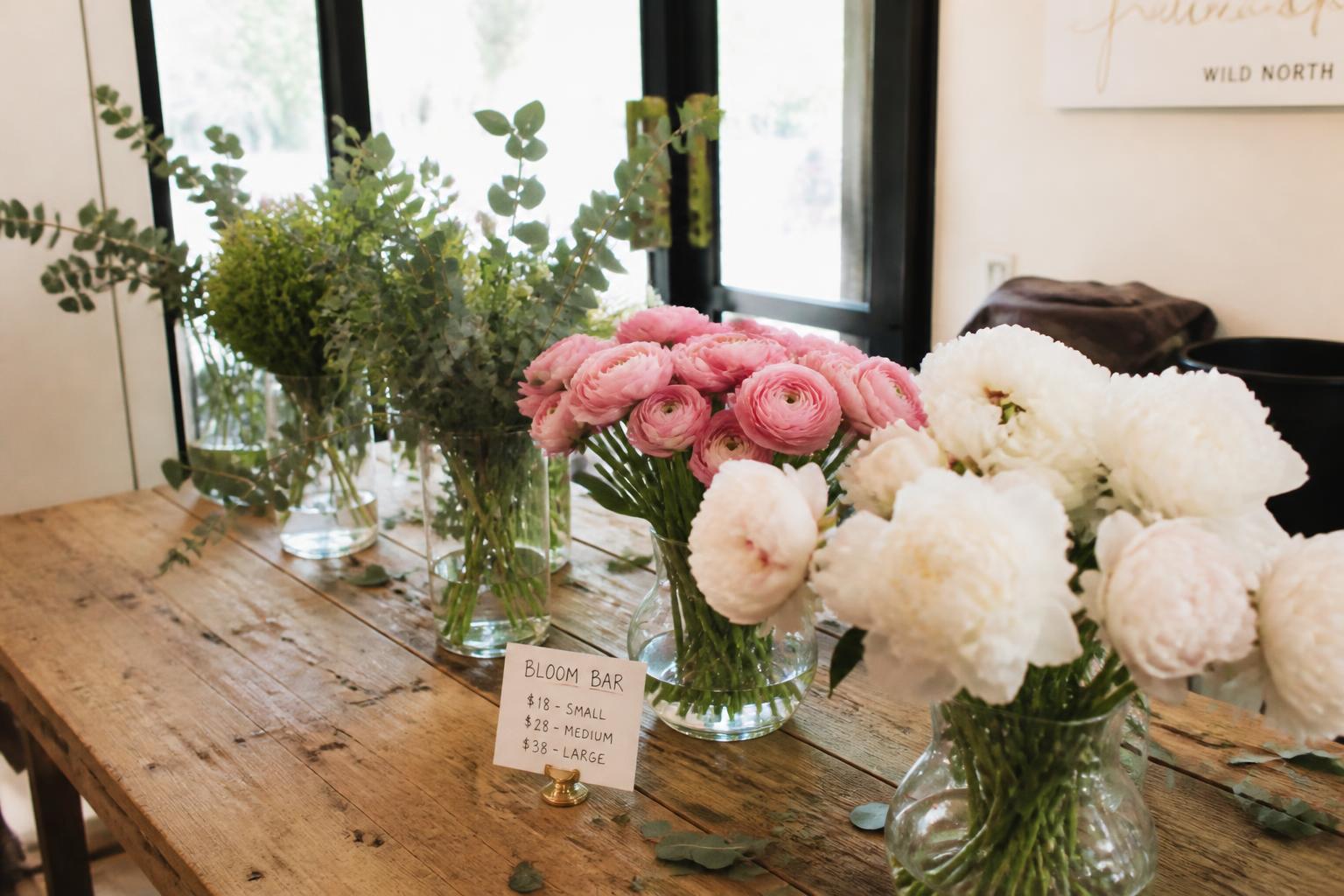 A bloom bar of pink ranunculus, white peonies and eucalyptus on a wooden table at golden hour